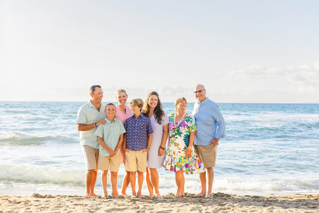 Parents and grandkids standing close and laughing on the sand with blue water during sunset
