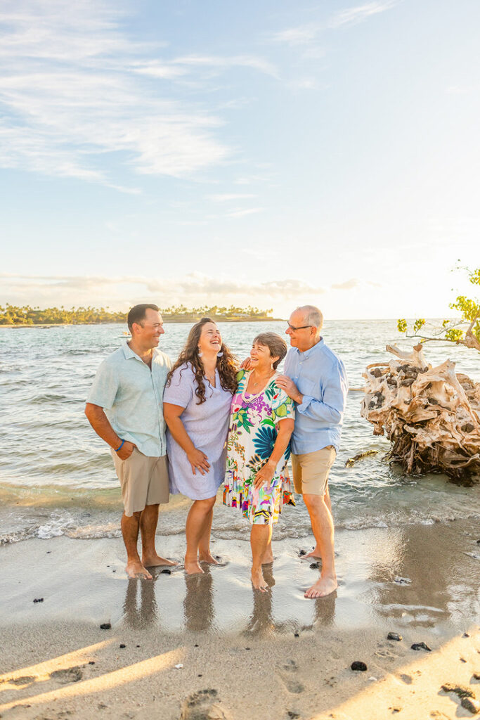 Parents holding hands with children at Mauna Lani beach with sand and driftwood during a sunset photoshoot 