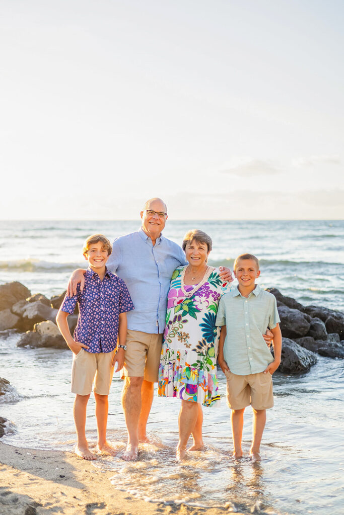 grandma, grandpa and grandkids smiling on the beach with feet in the water at sunset 