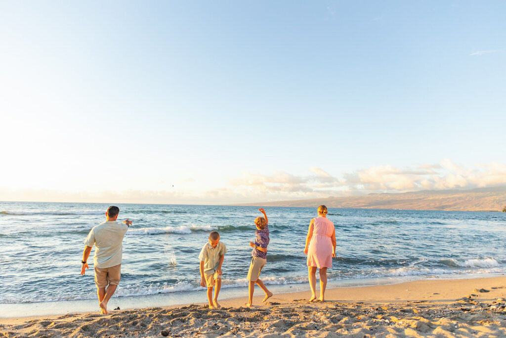 parents and kids skipping rocks into the ocean at mauna lani beach during golden hour