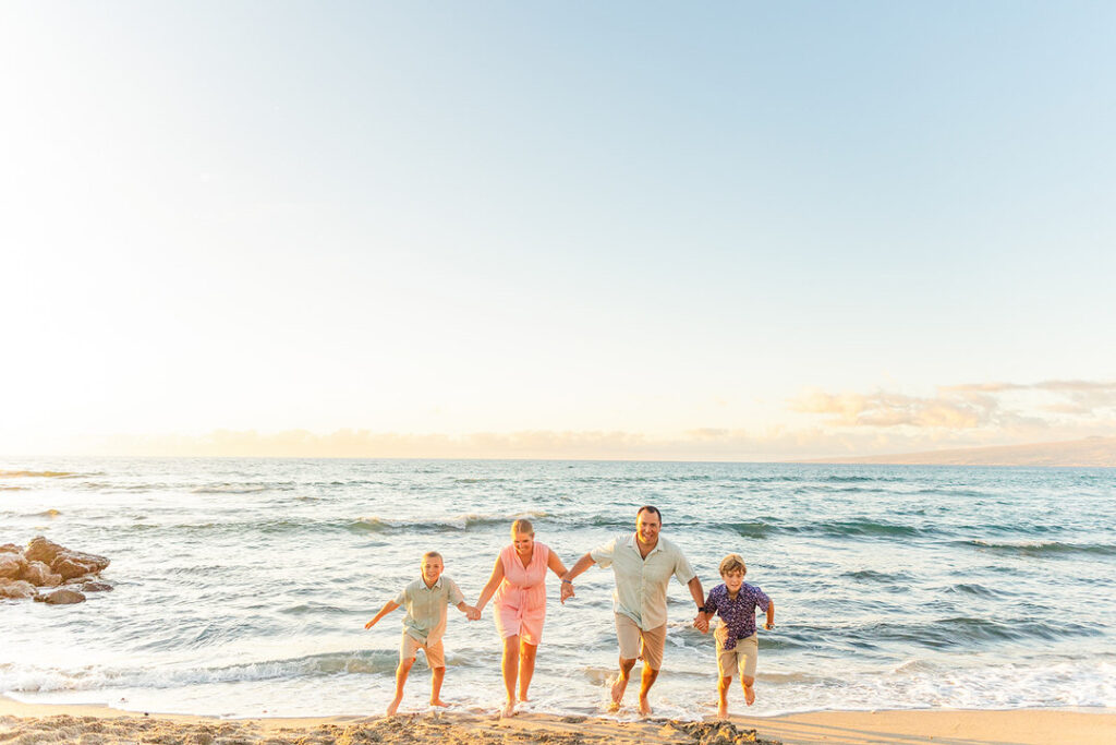 parents and kinds holding hand son the beach running out of the water at golden hour 