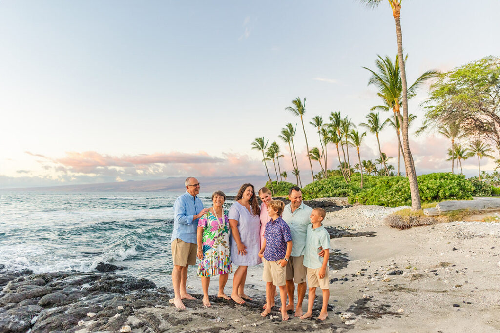 family laughing standing on lava rocks at Mauna Lani during golden hour surrounded by palm trees
